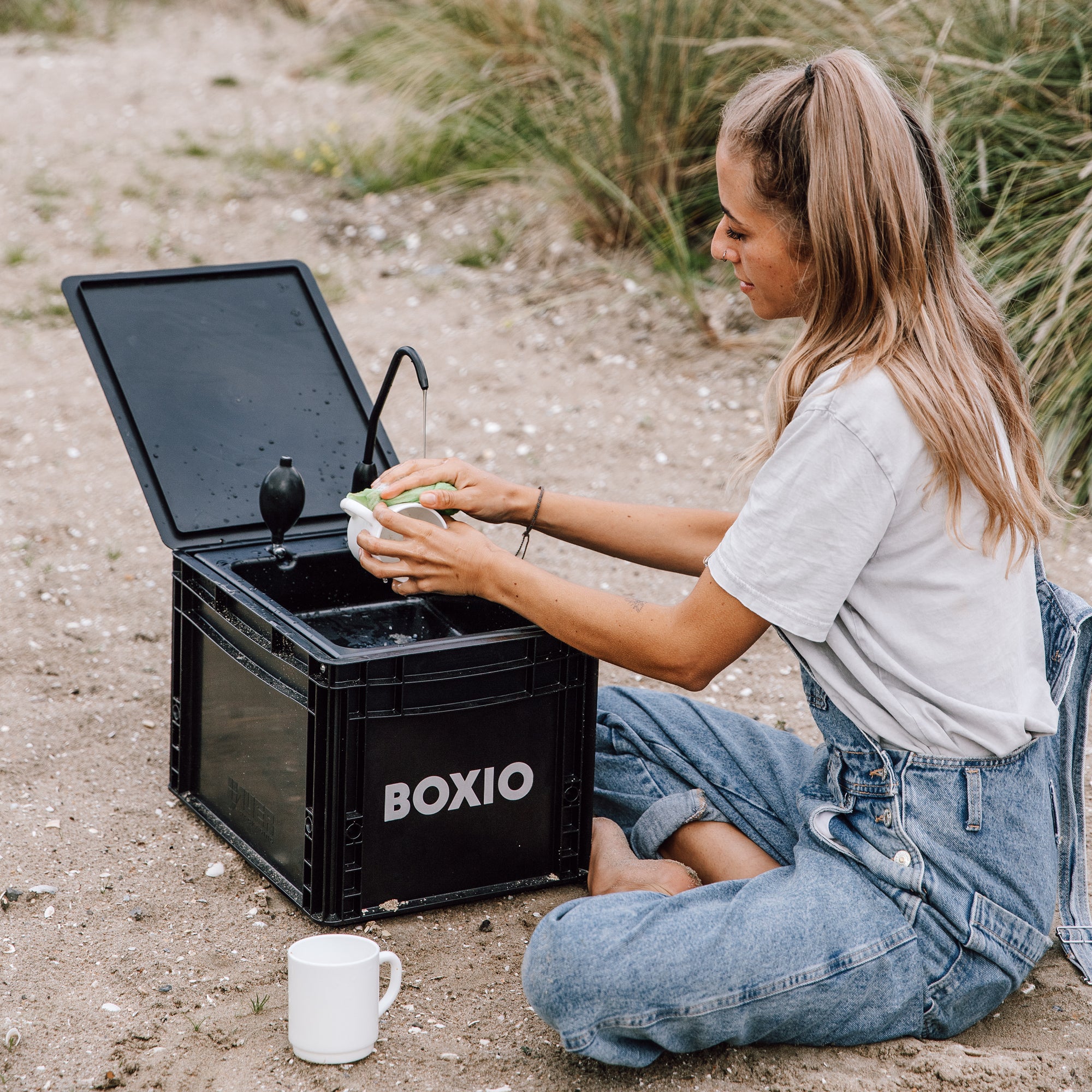 Woman washing hands at a BOXIO portable sink outdoors, showcasing the compact mobile bathroom solution.