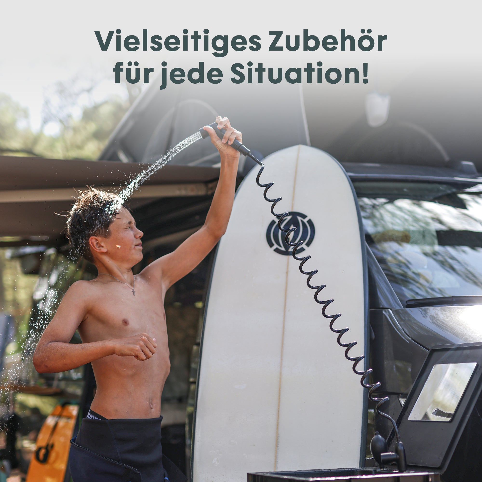 Junge spritzt Wasser mit einem flexiblen Schlauch neben einem Surfbrett und einem Fahrzeug.