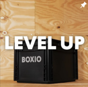 Schwarze Box mit dem Schriftzug "BOXIO" vor Holzpaneelen, darüber die Worte "LEVEL UP".