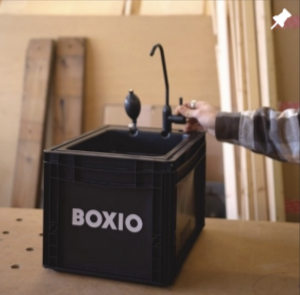 Tragbare Waschstation BOXIO mit Wasserhahn und Auffangbehälter auf einer Werkbank.